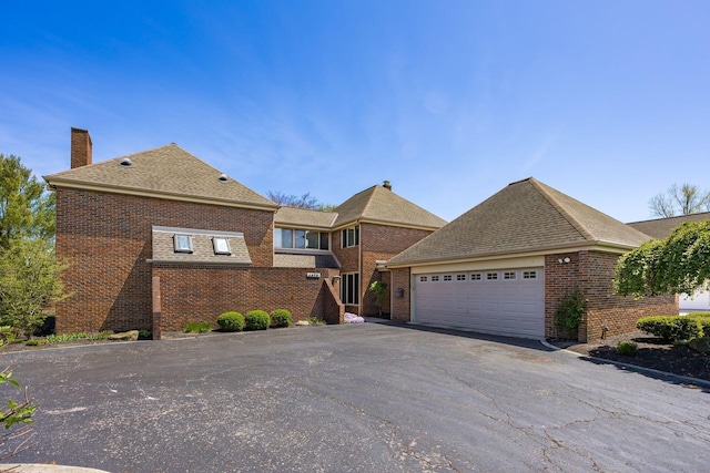 view of front of property featuring roof with shingles, an attached garage, brick siding, a chimney, and driveway