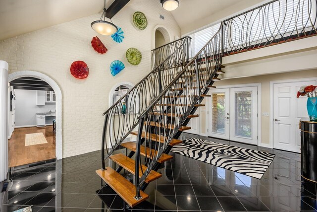 stairs with arched walkways, high vaulted ceiling, and granite finish floor