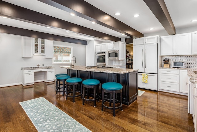 kitchen featuring light stone countertops, built in appliances, a breakfast bar area, an island with sink, and backsplash