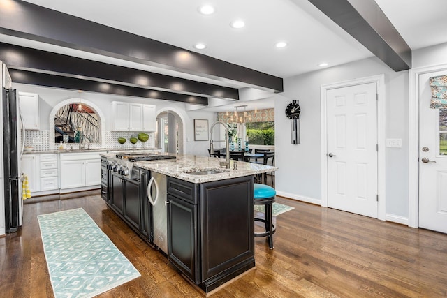 kitchen with a kitchen island with sink, a kitchen bar, white cabinetry, a sink, and appliances with stainless steel finishes