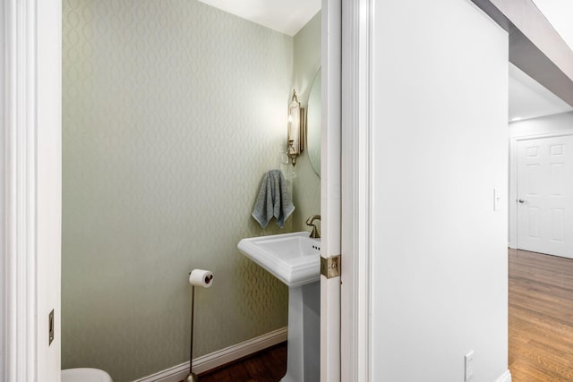 half bath with baseboards, a sink, wood finished floors, and wallpapered walls