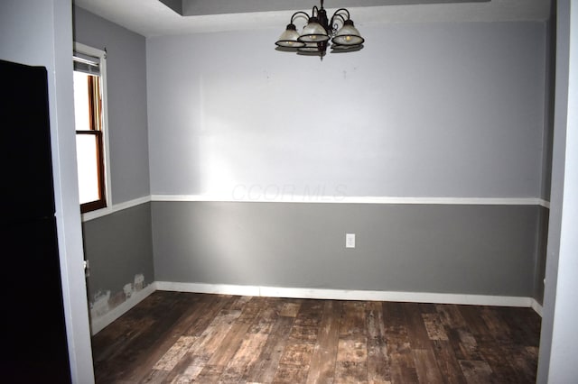 unfurnished dining area featuring baseboards, dark wood-style floors, and an inviting chandelier