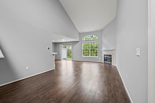 unfurnished living room featuring high vaulted ceiling, wood finished floors, a tiled fireplace, and baseboards