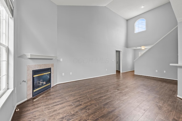 unfurnished living room featuring high vaulted ceiling, a fireplace, wood finished floors, and baseboards