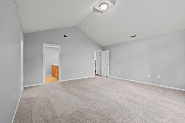 unfurnished bedroom with light colored carpet, vaulted ceiling, ensuite bathroom, and baseboards