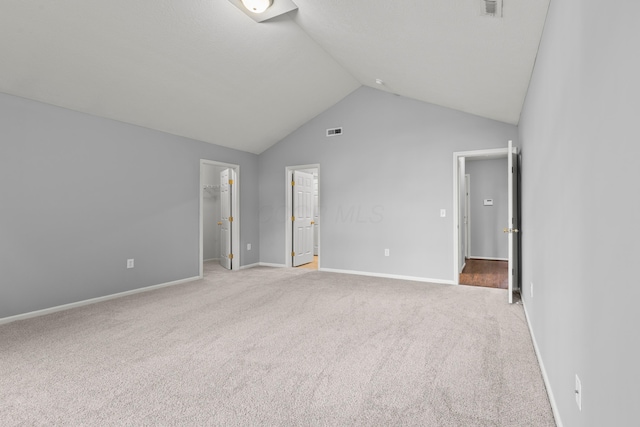 unfurnished bedroom featuring a walk in closet, light colored carpet, vaulted ceiling, baseboards, and a closet