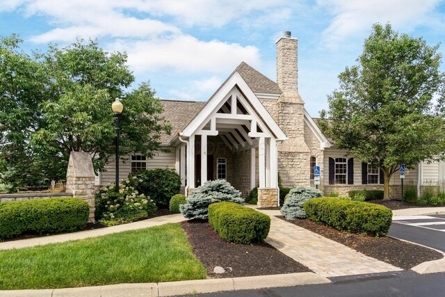 tudor-style house with stone siding, a chimney, and roof with shingles