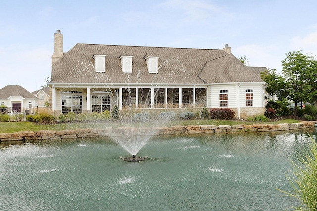 rear view of property with a chimney, fence, and a water view
