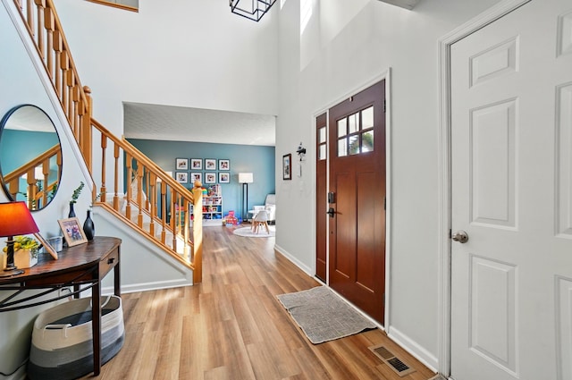 entrance foyer with a towering ceiling, visible vents, wood finished floors, baseboards, and stairs