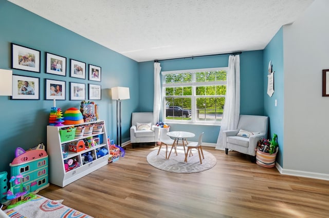 game room featuring baseboards, a textured ceiling, and wood finished floors