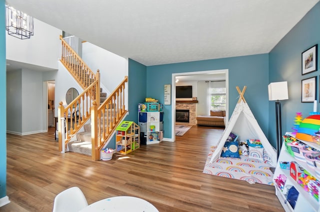 rec room with a stone fireplace, baseboards, and wood finished floors