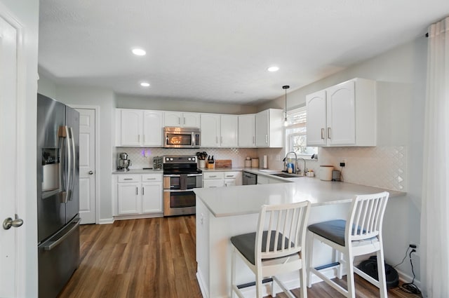 kitchen with dark wood-style flooring, appliances with stainless steel finishes, a sink, a peninsula, and backsplash