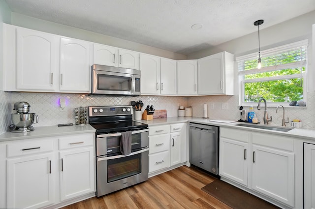 kitchen with decorative backsplash, a sink, white cabinets, stainless steel appliances, and light wood-style flooring
