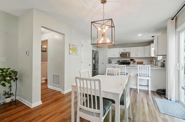 dining room featuring light wood-style floors, baseboards, a notable chandelier, and visible vents