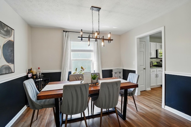 dining space with a textured ceiling, wood finished floors, and a notable chandelier