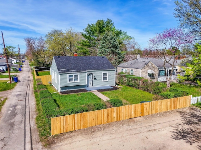 view of front of home with roof with shingles, a chimney, a front lawn, and fence