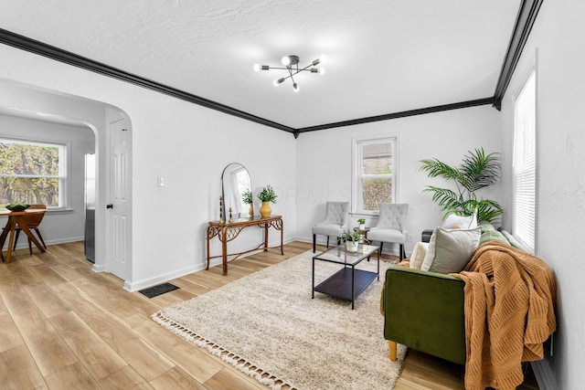 sitting room with arched walkways, light wood-style floors, baseboards, and ornamental molding