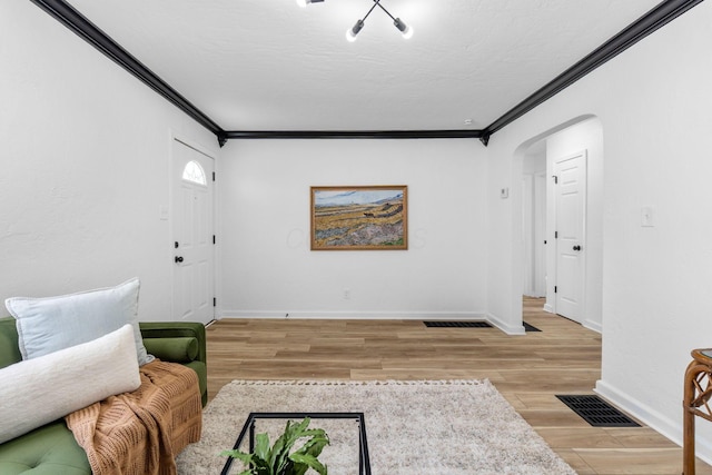 living room with arched walkways, crown molding, visible vents, and baseboards
