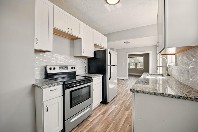 kitchen featuring white cabinets, a sink, light wood-style flooring, tasteful backsplash, and appliances with stainless steel finishes