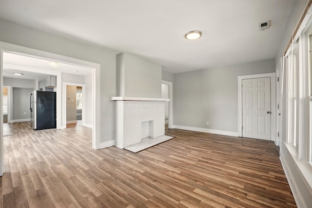 unfurnished living room featuring baseboards, a brick fireplace, and wood finished floors