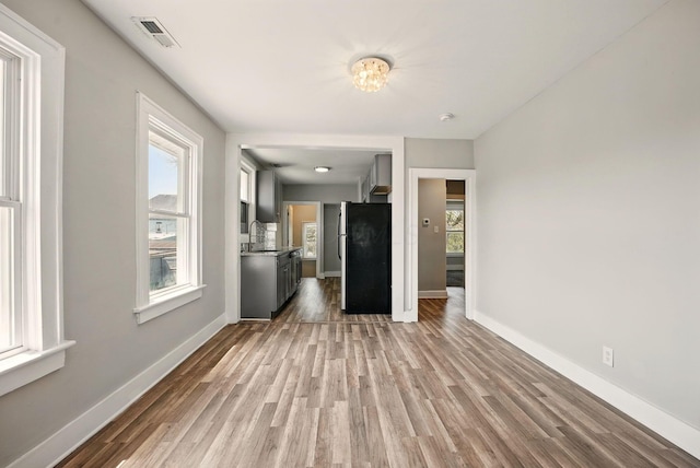 unfurnished living room with baseboards, wood finished floors, visible vents, and a sink