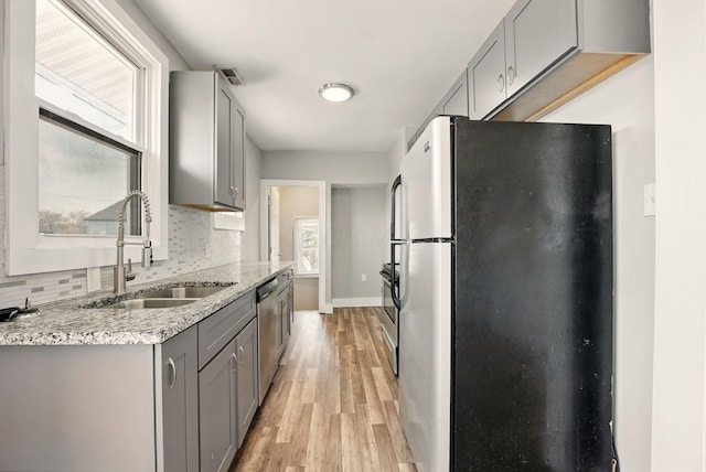 kitchen featuring tasteful backsplash, a sink, light wood-style floors, stainless steel appliances, and gray cabinetry