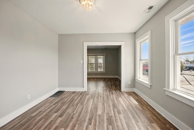 unfurnished room featuring wood finished floors, visible vents, and baseboards