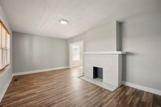 unfurnished living room featuring a brick fireplace, wood finished floors, a textured ceiling, and baseboards
