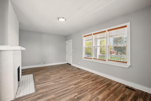 unfurnished living room with baseboards, wood finished floors, visible vents, and a brick fireplace