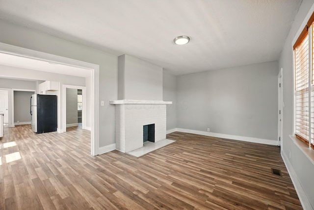 unfurnished living room featuring wood finished floors, a brick fireplace, baseboards, and visible vents