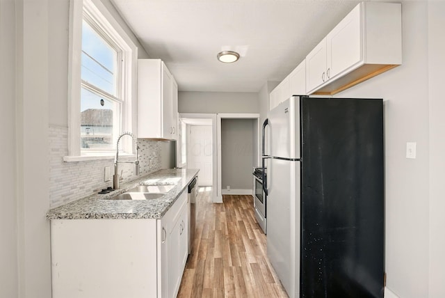 kitchen with light wood finished floors, stainless steel appliances, a sink, tasteful backsplash, and white cabinetry