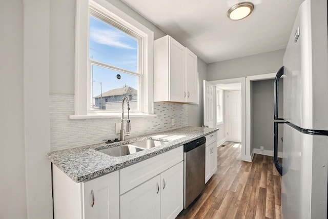 kitchen featuring white cabinets, a sink, freestanding refrigerator, wood finished floors, and dishwasher