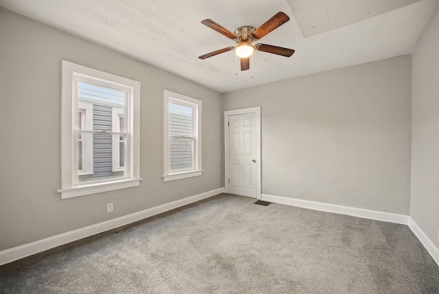 empty room with carpet floors, a ceiling fan, visible vents, and baseboards