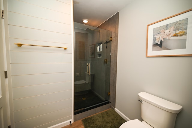 full bath with baseboards, wood finished floors, a shower stall, and toilet