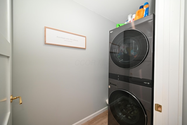 clothes washing area with baseboards, stacked washer and clothes dryer, wood finished floors, and laundry area