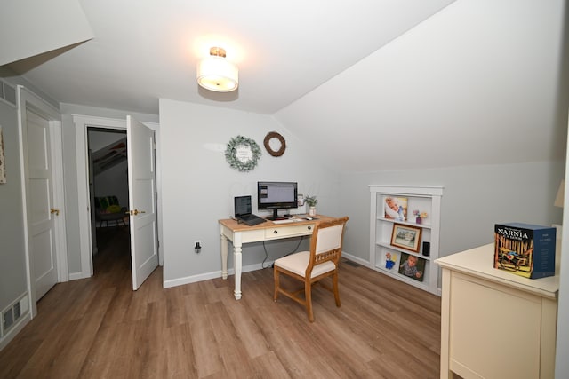 office featuring visible vents, baseboards, lofted ceiling, and light wood-style floors