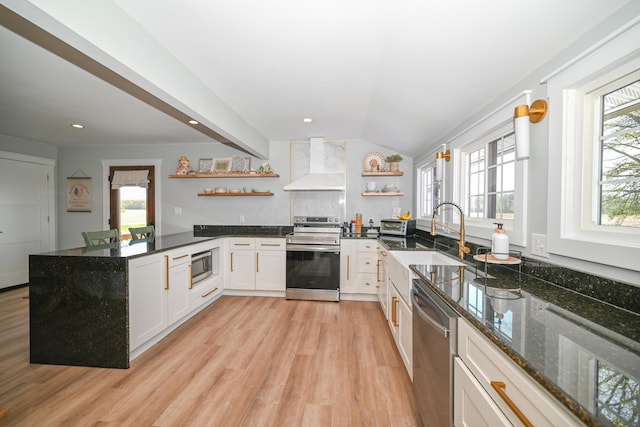 kitchen featuring stainless steel appliances, open shelves, wall chimney range hood, light wood-type flooring, and a peninsula
