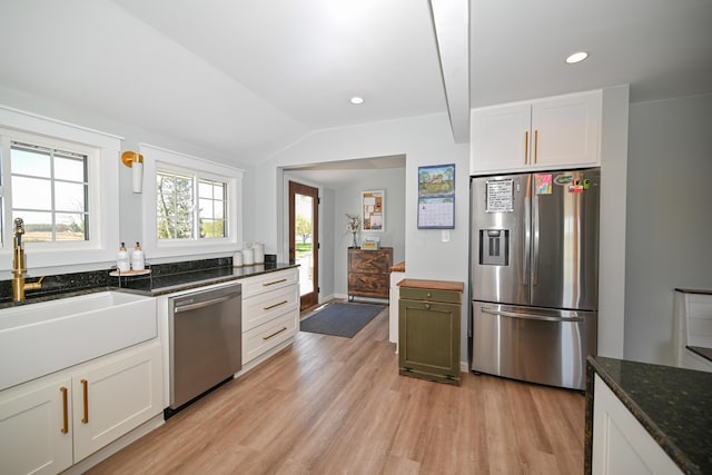 kitchen featuring lofted ceiling, dark stone counters, a sink, appliances with stainless steel finishes, and light wood finished floors