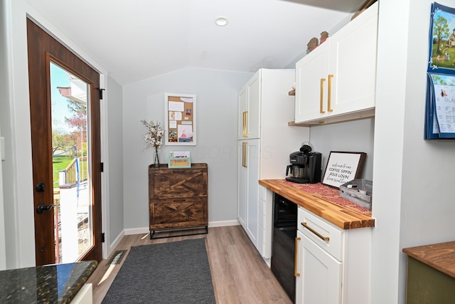 kitchen with wood counters, light wood-style floors, baseboards, white cabinets, and lofted ceiling