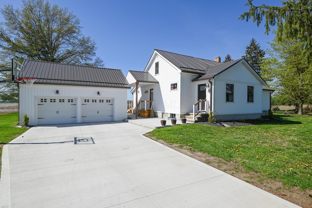 view of front of property featuring a front lawn, metal roof, an outbuilding, driveway, and a chimney