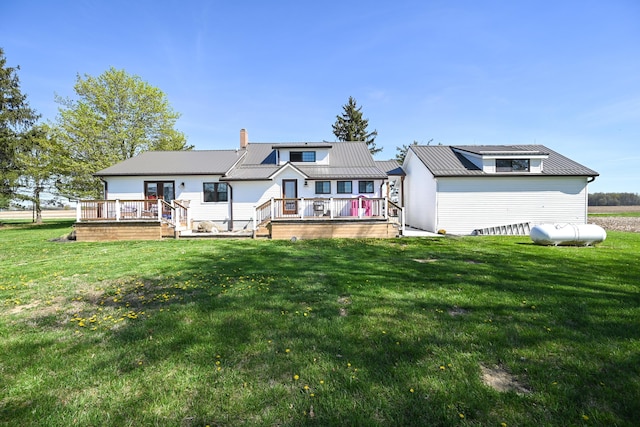 rear view of house with a deck, a chimney, metal roof, and a lawn