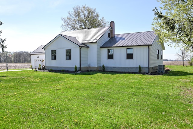 back of house featuring a garage, central AC unit, metal roof, a yard, and a chimney