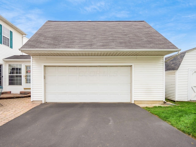 view of front of property with a storage shed, aphalt driveway, an outbuilding, and roof with shingles