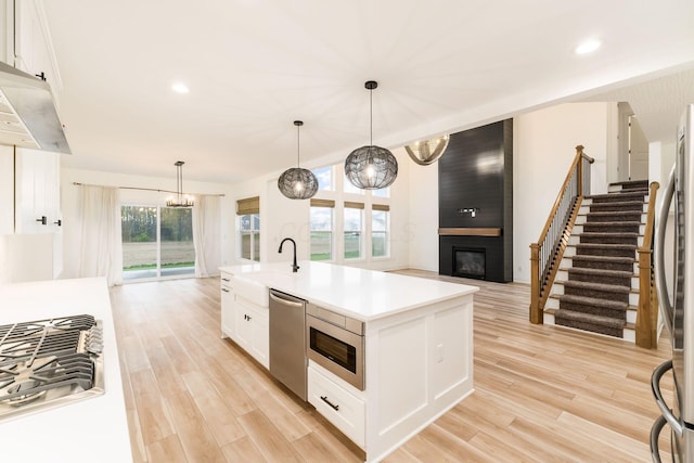 kitchen featuring a large fireplace, open floor plan, light wood-style flooring, and stainless steel appliances