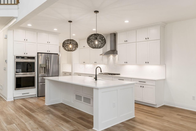 kitchen with light wood-style floors, backsplash, wall chimney range hood, light countertops, and appliances with stainless steel finishes