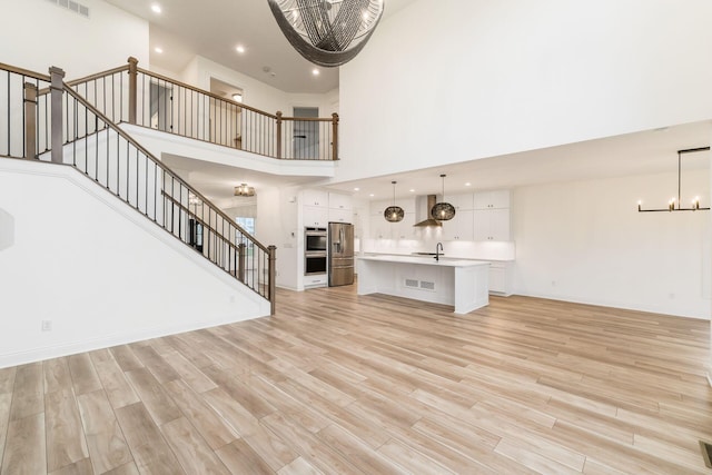 unfurnished living room with a chandelier, light wood-type flooring, a high ceiling, and stairway
