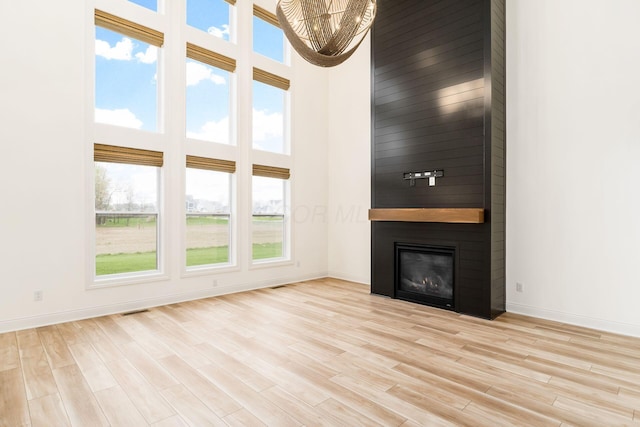 unfurnished living room with a fireplace, light wood-style floors, baseboards, and a high ceiling
