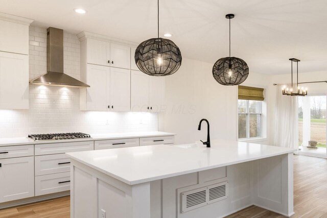 kitchen with tasteful backsplash, a kitchen island with sink, stainless steel gas stovetop, wall chimney range hood, and a sink
