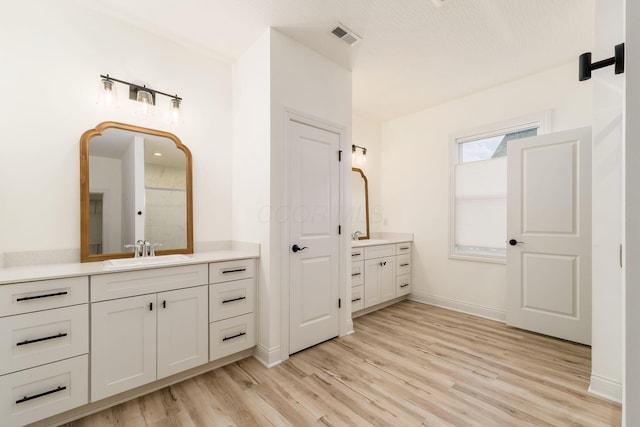 full bath featuring a sink, visible vents, baseboards, two vanities, and wood finished floors