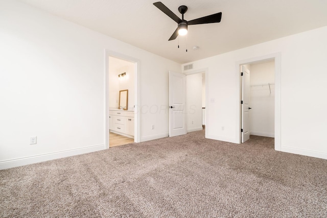 unfurnished bedroom with visible vents, ensuite bathroom, baseboards, light carpet, and a walk in closet
